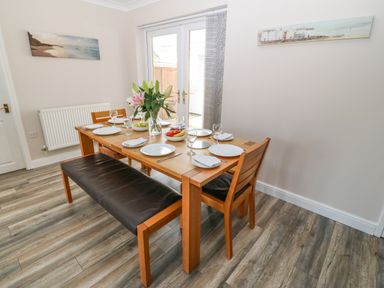 A dining area with a wooden table set for six with plates glasses and napkins with a black cushioned bench and chairs at St Winifreds in Rhosneigr