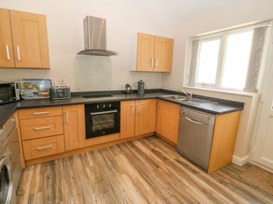A kitchen with wooden cabinets a black countertop and a stainless steel dishwasher by a window at St Winifreds in Rhosneigr