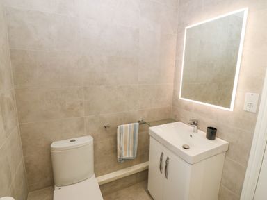 A bathroom with a toilet a sink with cabinet and a lit mirror at St Winifreds in Rhosneigr