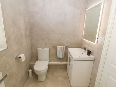 A bathroom with a toilet a sink with cabinet a towel rail and a lighted mirror at St Winifreds in Rhosneigr