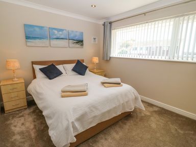 A bedroom with a large bed with white bedding and blue pillows two bedside tables with lamps and a triptych beach painting above the bed at St Winifreds in Rhosneigr