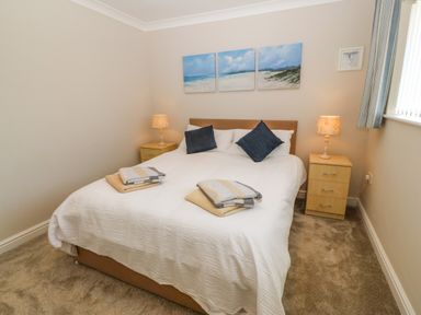 A bedroom with a double bed two bedside tables with lamps and three paintings above the bed at St Winifreds in Rhosneigr