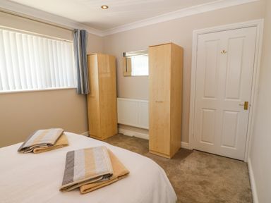 A bedroom with two wooden wardrobes a bed with folded towels a window with vertical blinds and a closed door at St Winifreds in Rhosneigr
