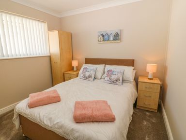 A bedroom with a double bed two wooden bedside tables with lamps a wooden wardrobe and a window with vertical blinds at St Winifreds in Rhosneigr