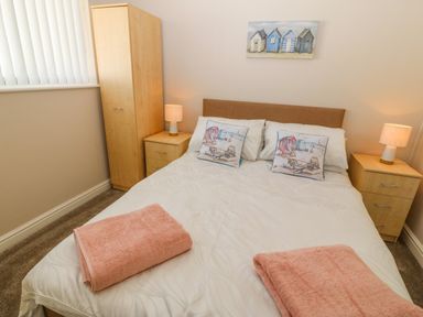 A bedroom with a double bed two bedside tables with lamps a wardrobe and paintings above the bed at St Winifreds in Rhosneigr