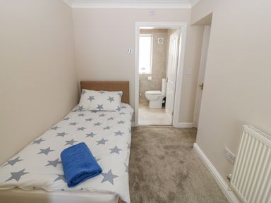 A small bedroom with a single bed with star-patterned bedding and a blue towel on top and an en suite bathroom in the background at St Winifreds in Rhosneigr