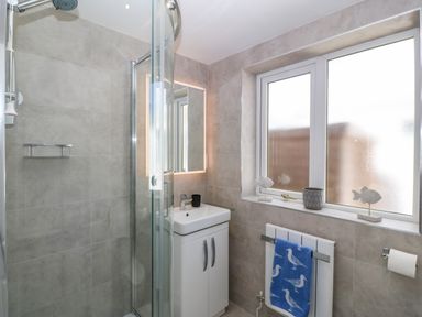 A bathroom with a shower cubicle sink cabinet window and radiator with a blue towel at St Winifreds in Rhosneigr