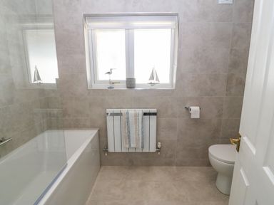 A bathroom with a bathtub a toilet a radiator with a towel and a window with decorations at St Winifreds in Rhosneigr