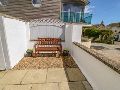 A wooden bench on a gravel area with two potted plants against a white wall outside a house at St Winifreds in Rhosneigr