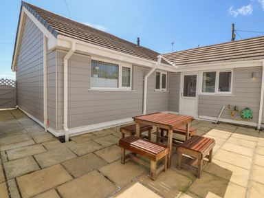 An outdoor patio area with beige paving stones and wooden table with benches at St Winifreds in Rhosneigr