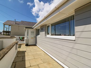 An outdoor patio area with stone tiles white walls a grey siding house and a white door at St Winifreds in Rhosneigr