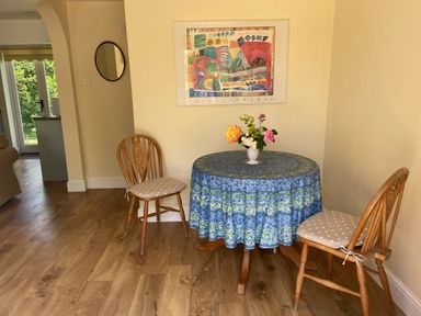 A small dining area with a round table covered by a blue tablecloth and two wooden chairs with cushions at Oke Apple Cottage in Okeford Fitzpaine