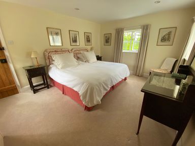 A bedroom with a double bed bedside tables lamps framed pictures and a window at Oke Apple Cottage in Okeford Fitzpaine