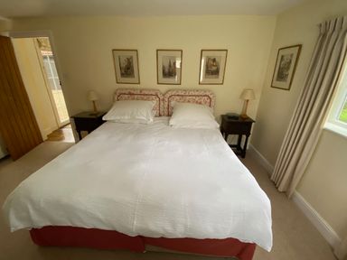 A bedroom with a double bed white duvet two pillows bedside tables with lamps and framed pictures on the wall at Oke Apple Cottage in Okeford Fitzpaine