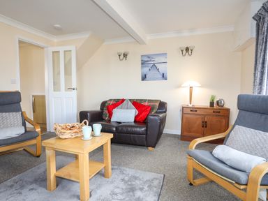 A living room with a leather sofa two armchairs a wooden coffee table and a wooden cabinet at Glan Y Don Bach in Abersoch
