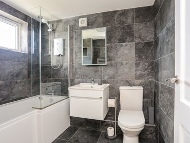 A bathroom with a bathtub shower combination a white sink and a toilet at Glan Y Don Bach in Abersoch