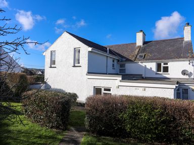 A white two-story house with a black roof and trimmed bushes in the garden at Glan Y Don Bach in Abersoch