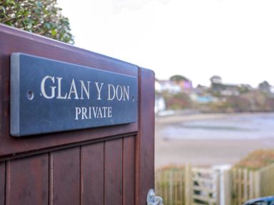 A wooden gate with a sign reading Glan Y Don Private with a beach and houses visible in the background at Glan Y Don Bach in Abersoch