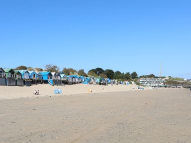 A sandy beach with colorful beach huts and some people sitting and walking at Glan Y Don Bach in Abersoch