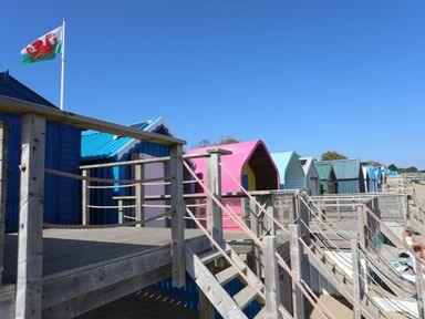 A row of colorful beach huts with wooden walkways and a flagpole flying the Welsh flag at Glan Y Don Bach in Abersoch