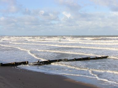 A beach with waves crashing against wooden groynes and a cloudy sky at Beach Cottage in Conwy