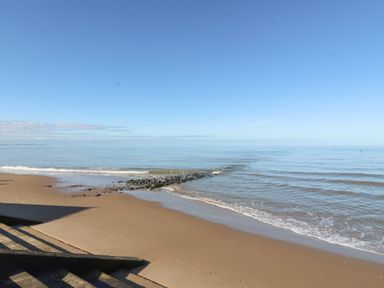 A sandy beach with steps leading down to the shore and a rock jetty extending into the sea at Beach Cottage in Conwy