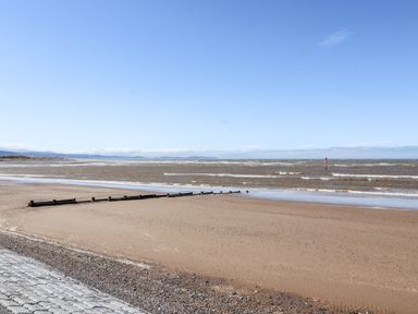 A sandy beach with wooden groynes and a calm sea under a clear blue sky at Beach Cottage in Conwy