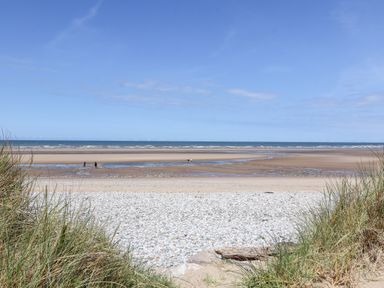A beach with grass in the foreground, pebbles, sand and people near the water at Beach Cottage in Conwy
