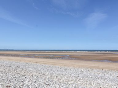A beach with pebbles and sand leading to the sea under a blue sky at Beach Cottage in Conwy