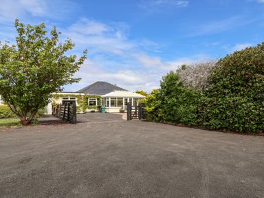 A house with a conservatory and driveway surrounded by trees and bushes at Beach Cottage in Conwy