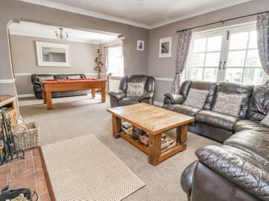 A living room with leather sofas a wooden coffee table a pool table and a fireplace at Beach Cottage in Conwy