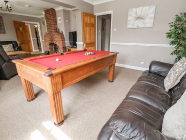 A living room with a red pool table a brown leather sofa a brick fireplace and a television at Beach Cottage in Conwy