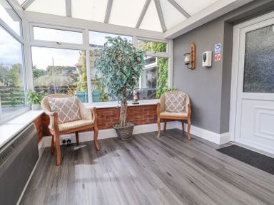 A sunroom with two wicker chairs with cushions a potted plant and a door at Beach Cottage in Conwy