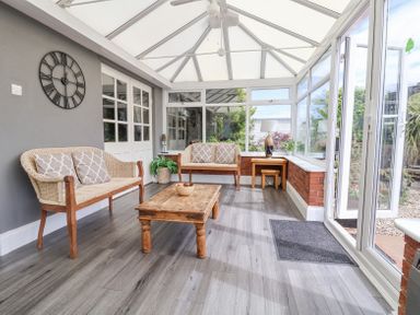 A conservatory with two wicker sofas a wooden coffee table a side table with a lamp and a clock on the wall at Beach Cottage in Conwy