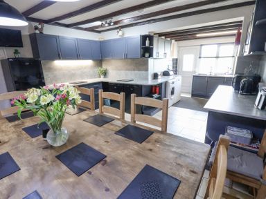 A kitchen with wooden dining table and chairs and dark cabinets at Beach Cottage in Conwy