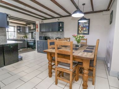 A dining area with wooden table and chairs next to a kitchen with dark cabinets and appliances at Beach Cottage in Conwy