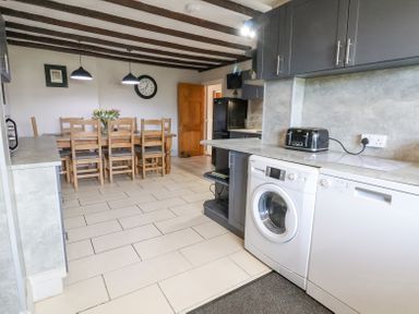 A kitchen with a washing machine dishwasher toaster dining table chairs and wooden ceiling beams at Beach Cottage in Conwy