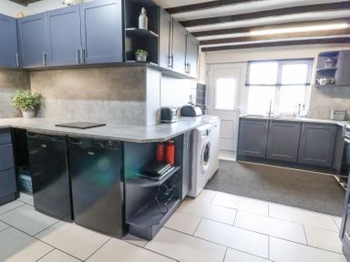 A kitchen with dark blue cabinets a washing machine two black fridges a countertop plant and a window at Beach Cottage in Conwy
