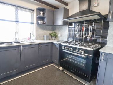 A kitchen with dark cabinets a gas stove cookware hanging on the wall and a window over the sink at Beach Cottage in Conwy