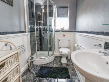 A bathroom with a shower, toilet, sink, and a wicker storage unit at Beach Cottage in Conwy