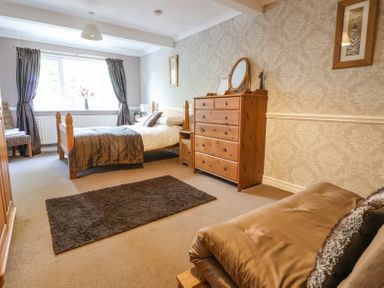 A bedroom with a wooden bed a dresser a brown rug and a chair by the window at Beach Cottage Conwy