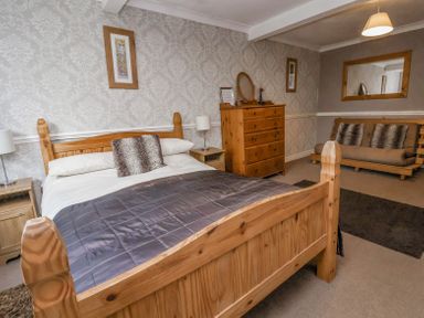 A bedroom with a wooden bed and dresser and a sofa with cushions at Beach Cottage in Conwy