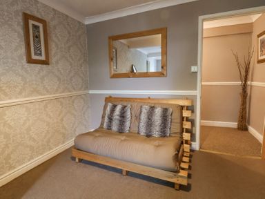 A small room with a wooden framed futon sofa bed two pillows a wall mirror and a framed zebra picture at Beach Cottage in Conwy