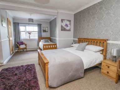 A bedroom with two wooden beds a purple rug a chair with towels and floral paintings at Beach Cottage in Conwy