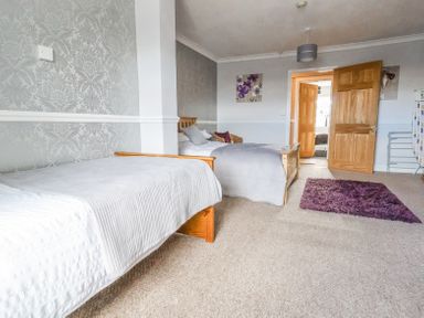 A bedroom with two wooden beds a purple rug and doors leading to another room at Beach Cottage in Conwy