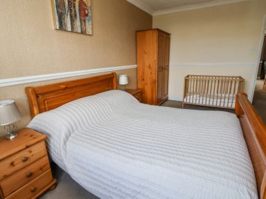 A bedroom with a wooden bed and bedside tables a wardrobe and a baby crib at Beach Cottage in Conwy