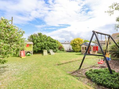 A garden with children's play equipment including a slide a playhouse and a swing set with two chairs in the background at Beach Cottage in Conwy
