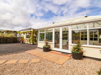 A conservatory with glass doors and windows attached to a house with a gravel and paved path outside at Beach Cottage in Conwy