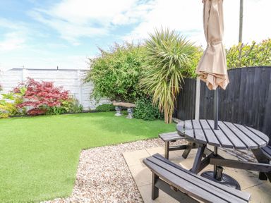 A garden with artificial grass a wooden picnic table with an umbrella and a stone bench at Beach Cottage in Conwy
