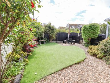 A garden with a lawn and gravel path with shrubs and a picnic table at Beach Cottage in Conwy